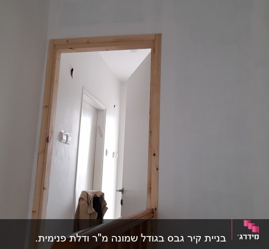 קיר גבס צבוע בלבן עם מסגרת עץ לדלת